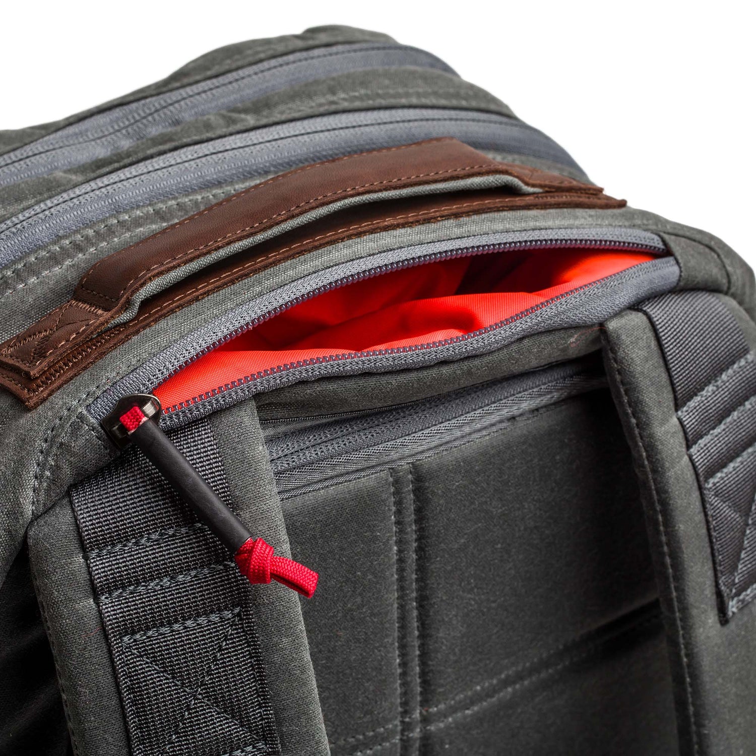 Close-up of the Double Compartment Bullet Ruck - Heritage Waxed Canvas - 18L in gray, featuring a red-lined pocket partially unzipped and sturdy shoulder straps.