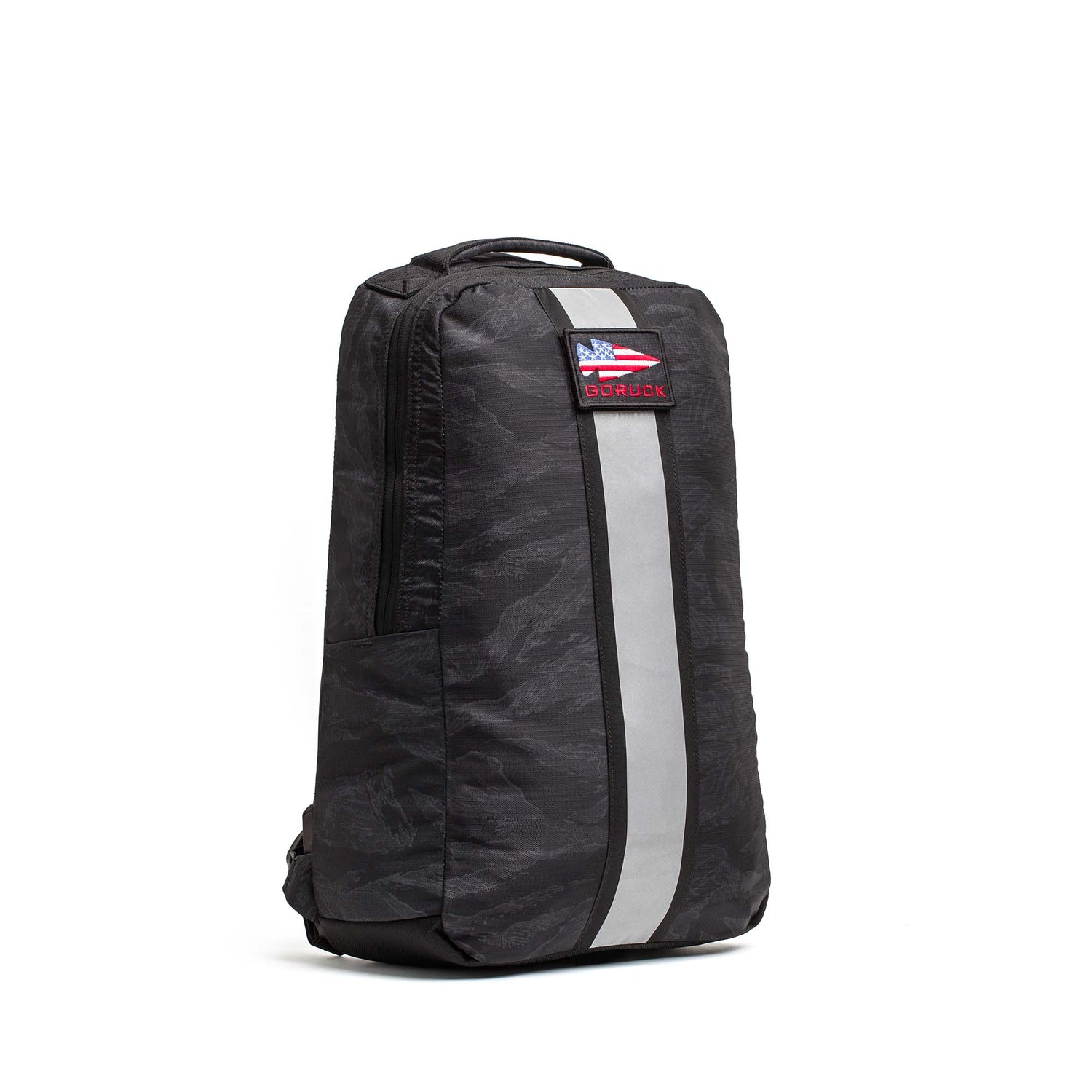The Basic Rucker is a black backpack with a gray reflective stripe, top handle, and an American flag patch with