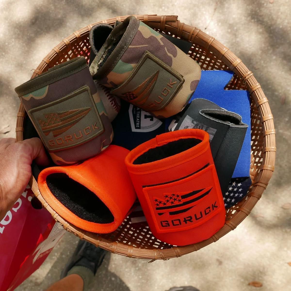 GORUCK beer jackets in camo, orange, and black designs in a basket outdoors