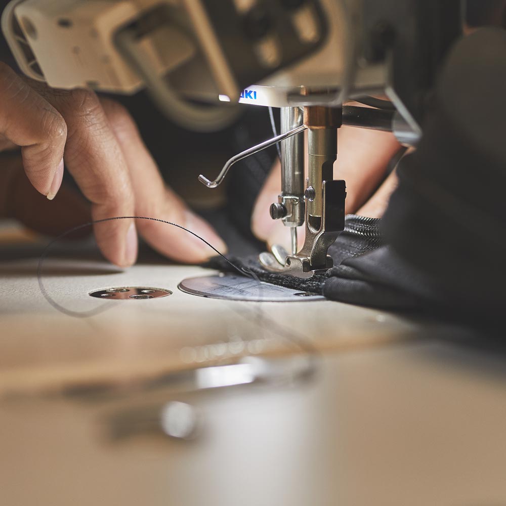 Close-up of hands guiding fabric through a sewing machine with visible needle and thread.