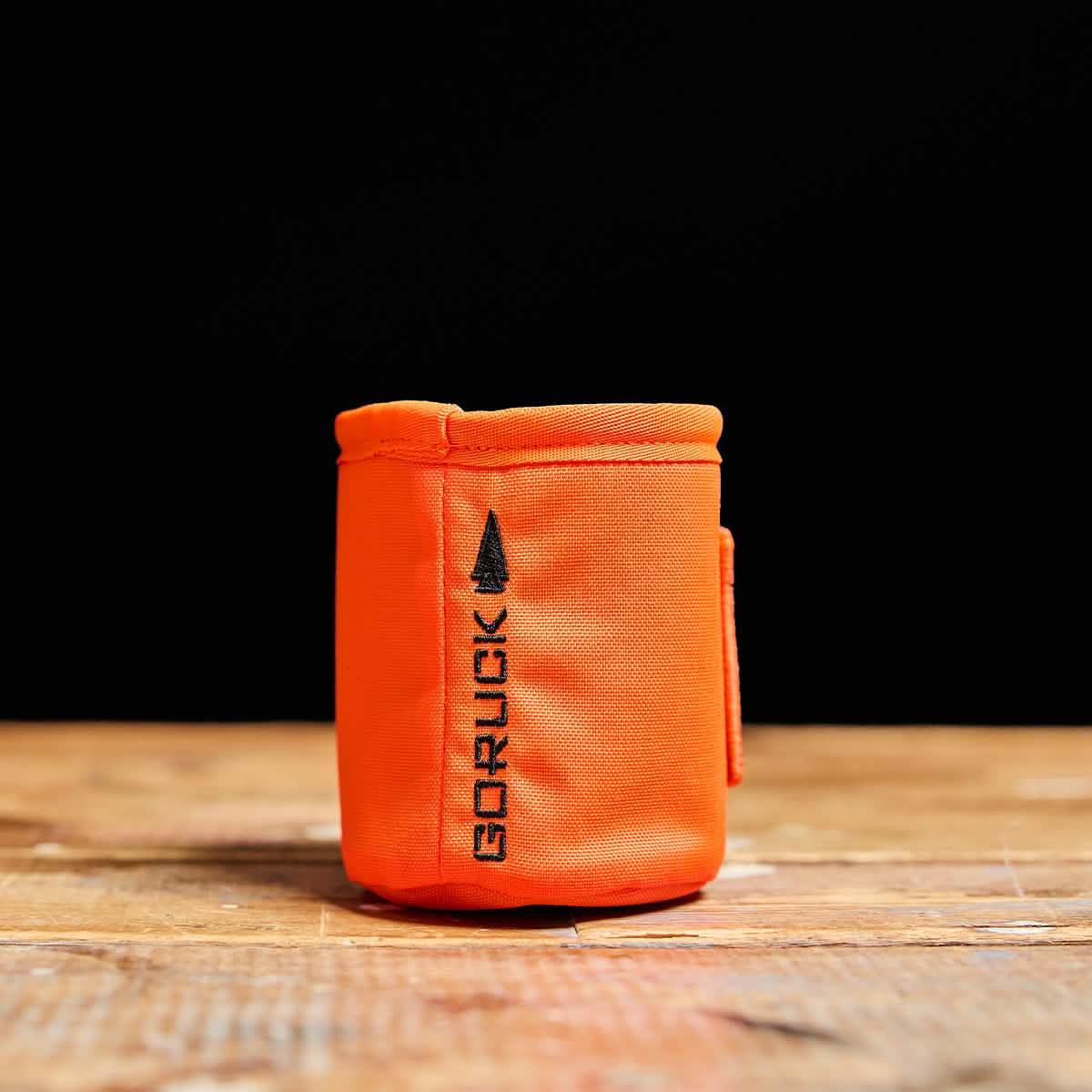 GORUCK orange beer jacket can cooler on wood surface, rugged outdoor gear accessory