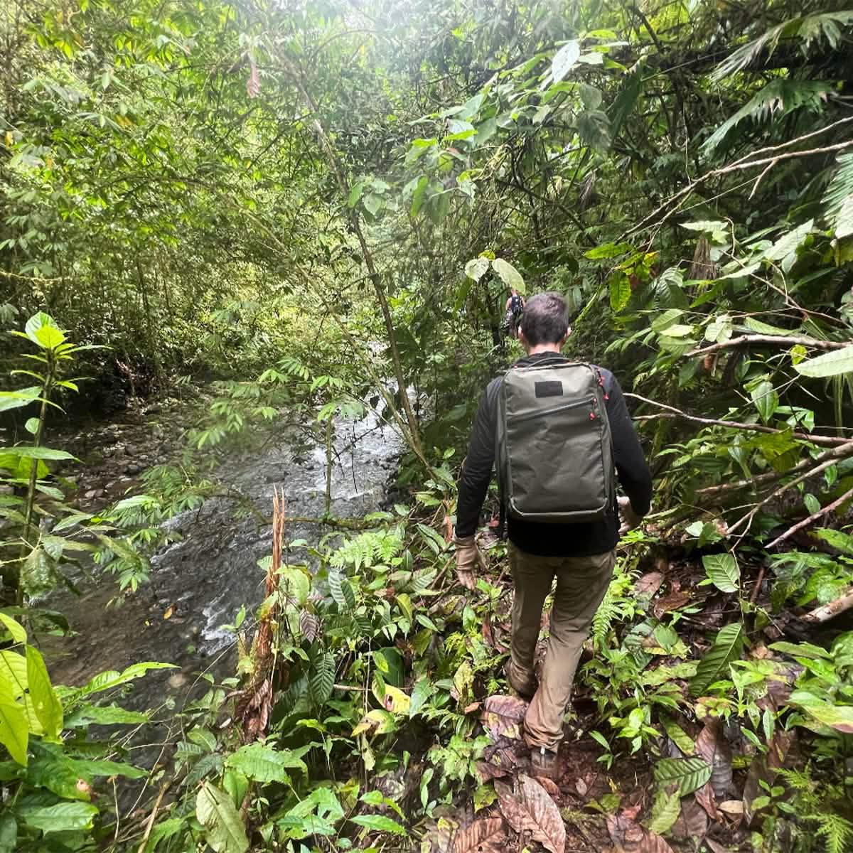Man hiking with GORUCK backpack on jungle trail beside river