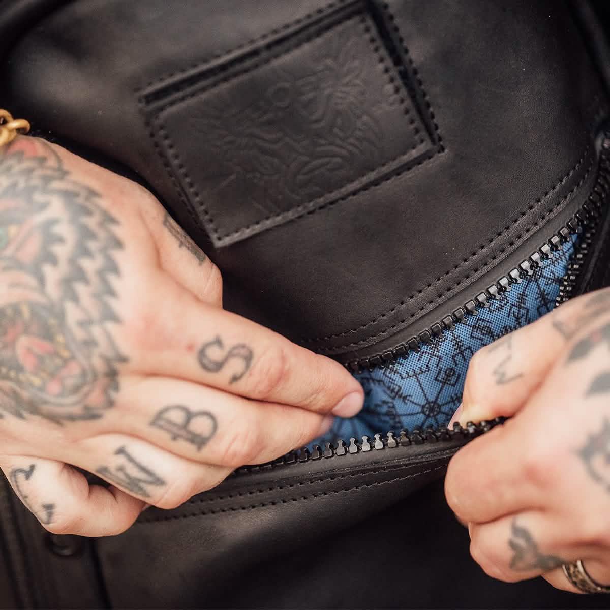 Tattooed hands opening GORUCK black rucking gear pocket with blue interior lining
