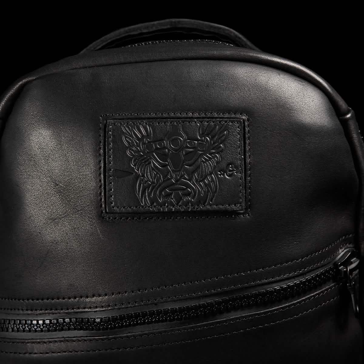 Close-up of GORUCK black leather rucksack with embossed patch and front zipper pocket