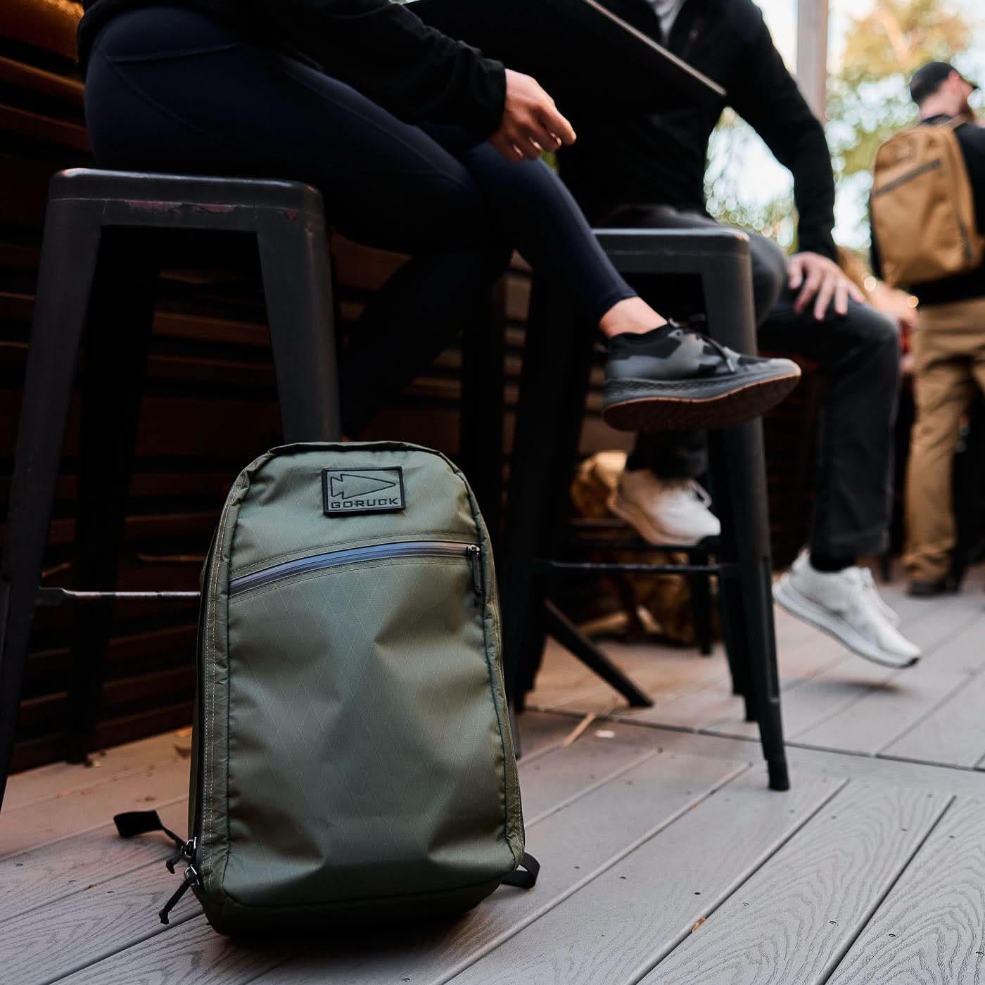 GORUCK green rucksack on floor beside people seated outdoors in casual gear