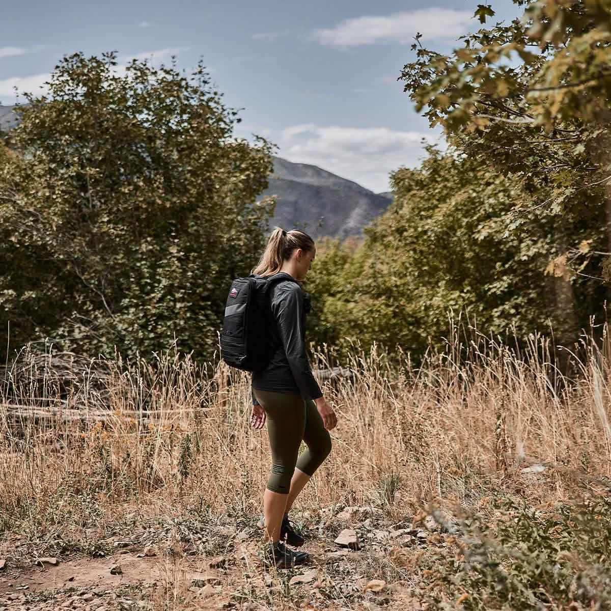 Woman rucking outdoors in GORUCK cropped leggings and black backpack in a scenic nature setting