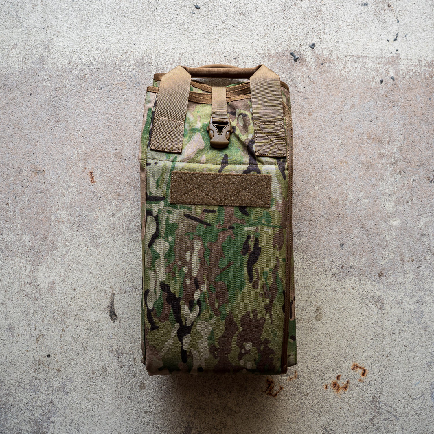 A folded camouflage Shooting Mat with tan straps rests on a textured concrete surface.