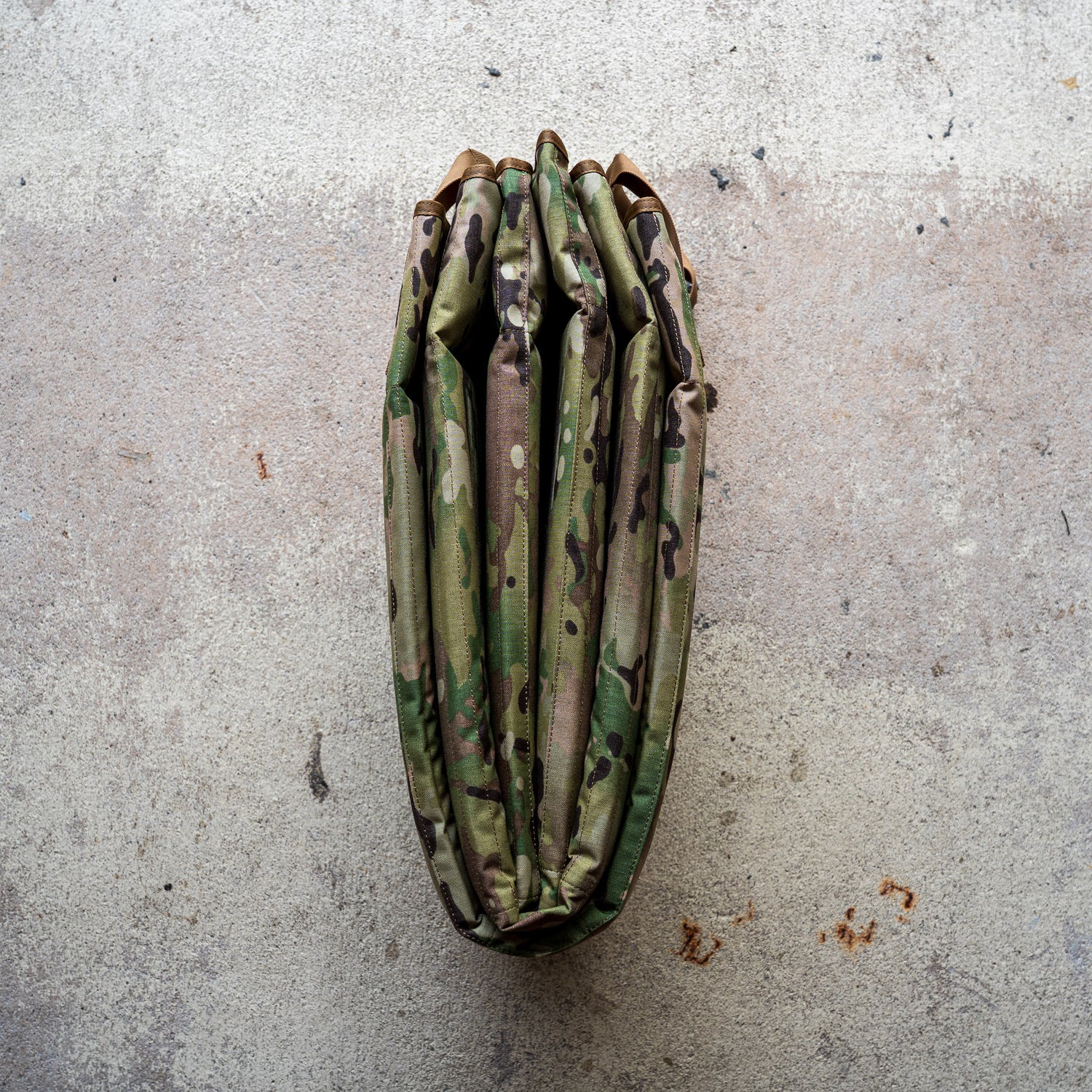 A folded Shooting Mat with a camouflage pattern rests on a rough, light-colored concrete surface.