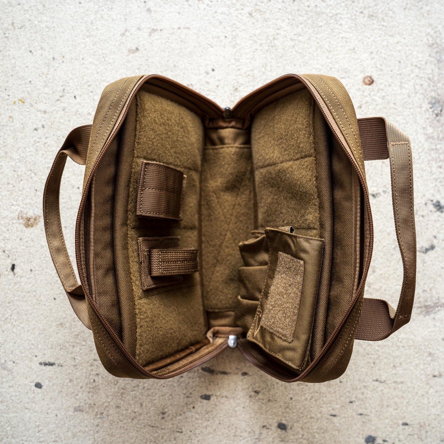 A brown Pistol Rug with compartments and straps lies open on a light, speckled surface.