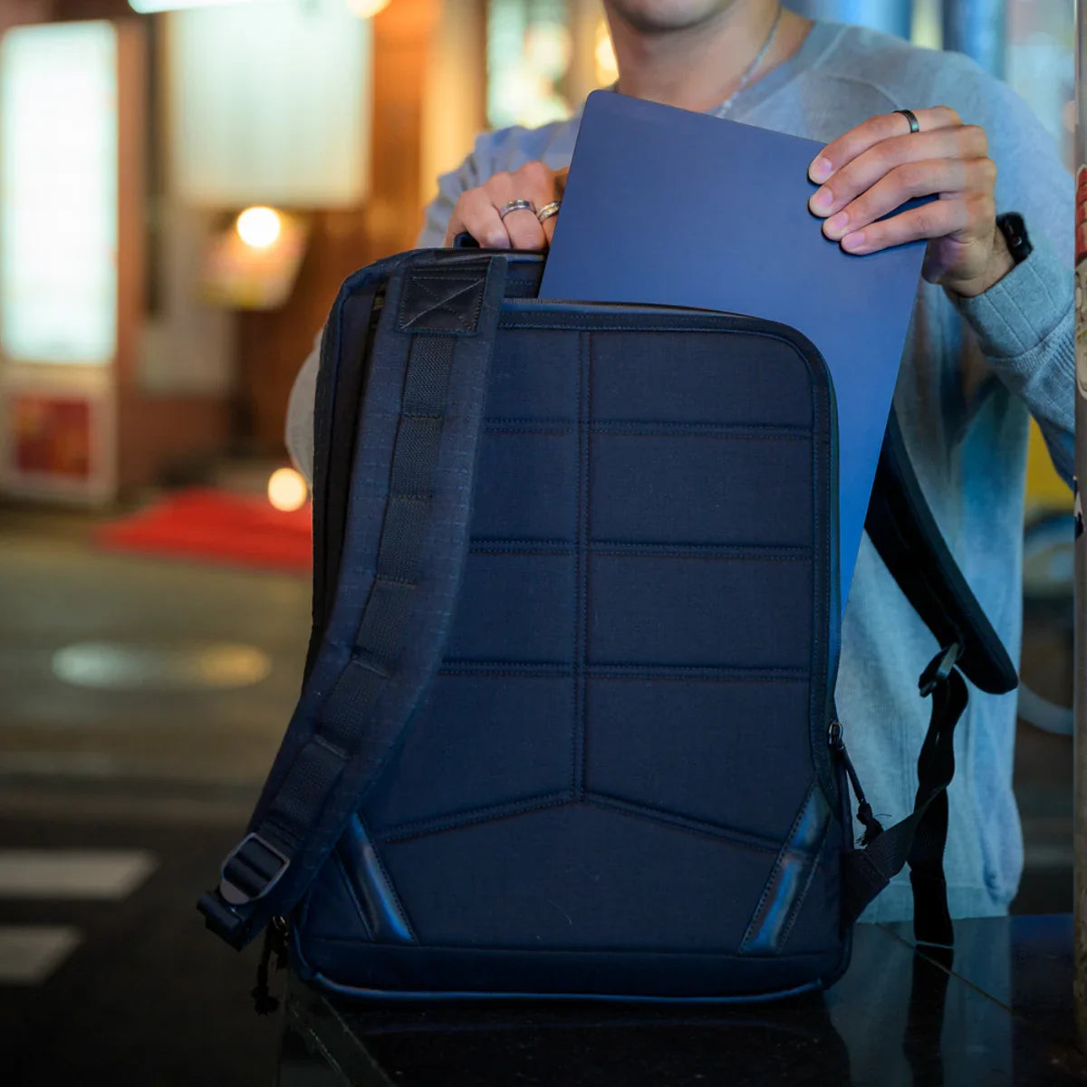 Person placing laptop into GORUCK backpack at night, showcasing durable rucking gear