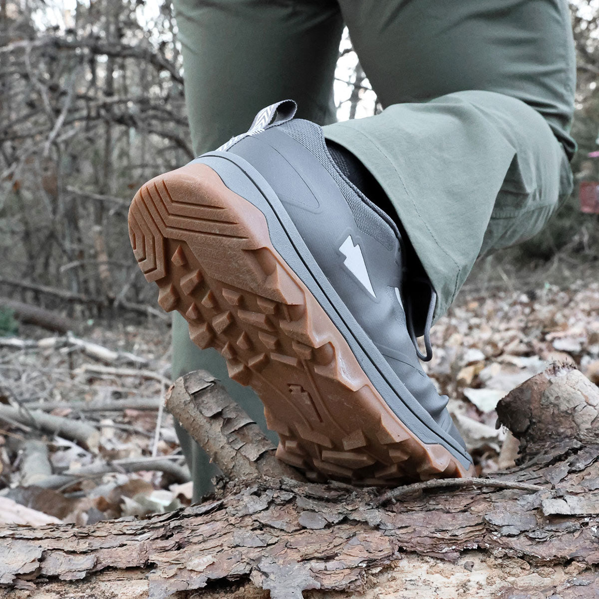 Close-up of a person stepping on a fallen log in the woods, showing the tread of a hiking shoe.