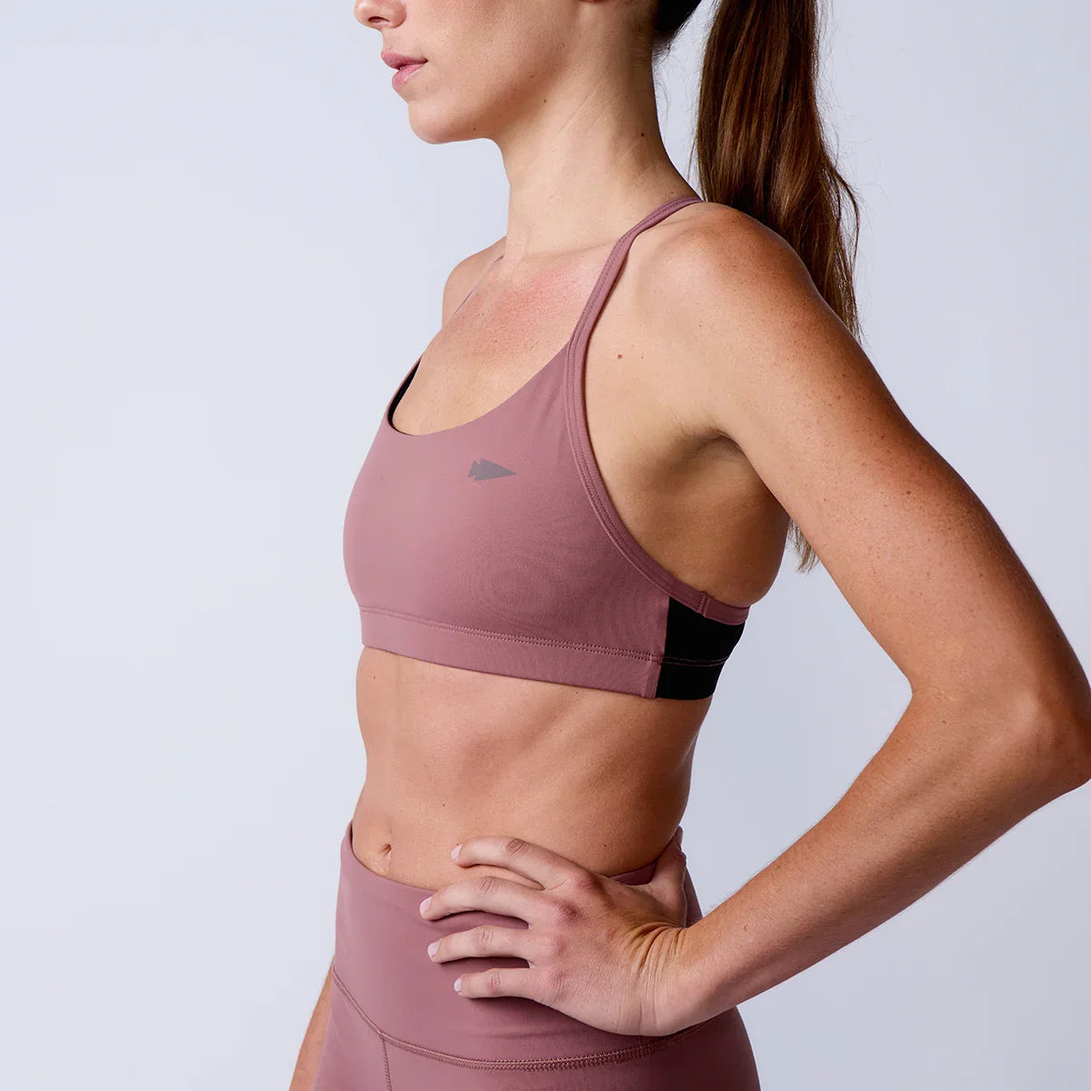 Woman wearing mauve GORUCK sports bra and leggings in studio, side profile view