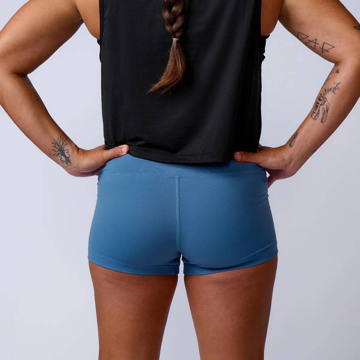 Back view of woman in blue GORUCK athletic shorts, black tank top, and visible arm tattoos