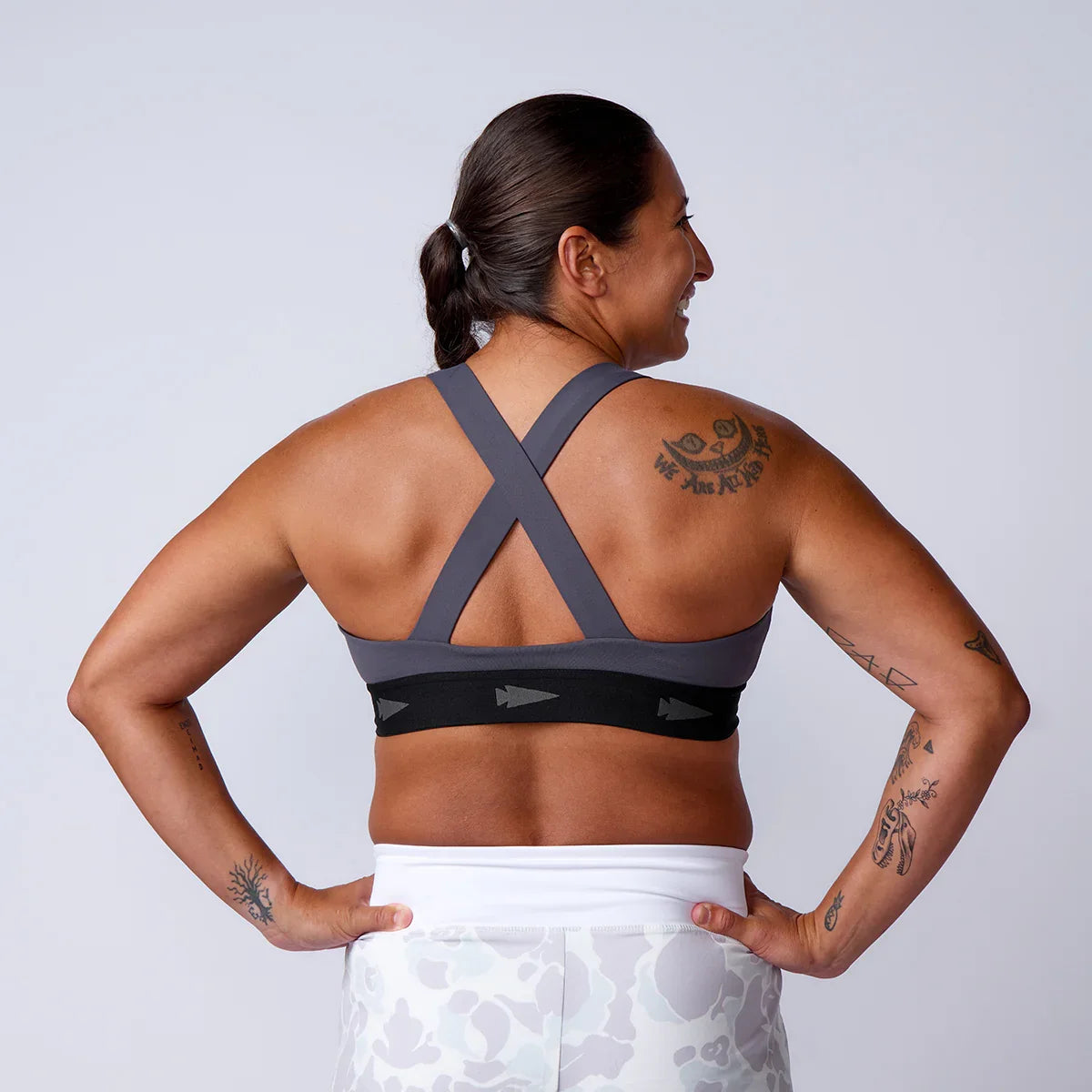 GORUCK athletic woman showing gray sports bra with crossed straps and black band, tattoos visible