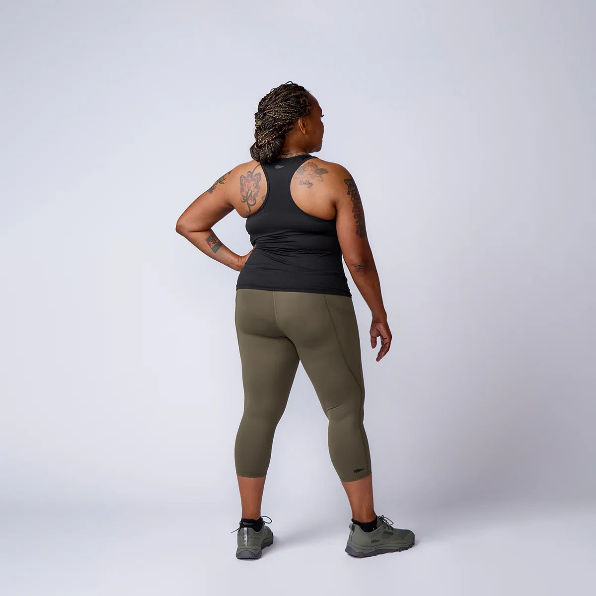 Woman in athletic GORUCK gear, black tank top, olive leggings, and sneakers, studio background