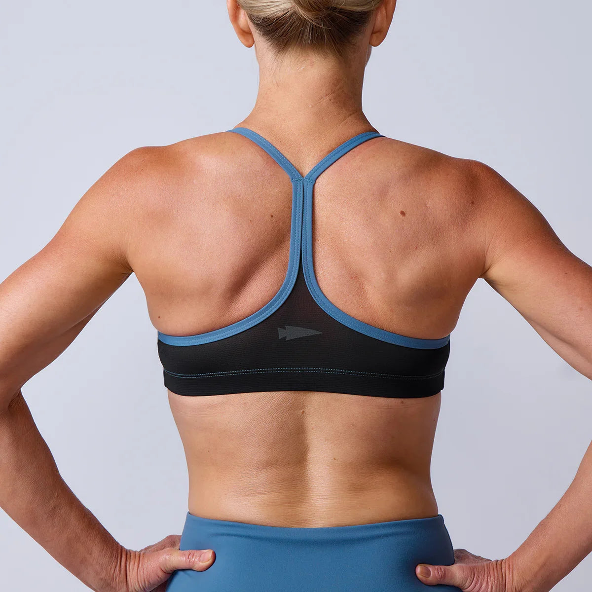Woman wearing GORUCK athletic sports bra and leggings, back view, fitness gear studio shot