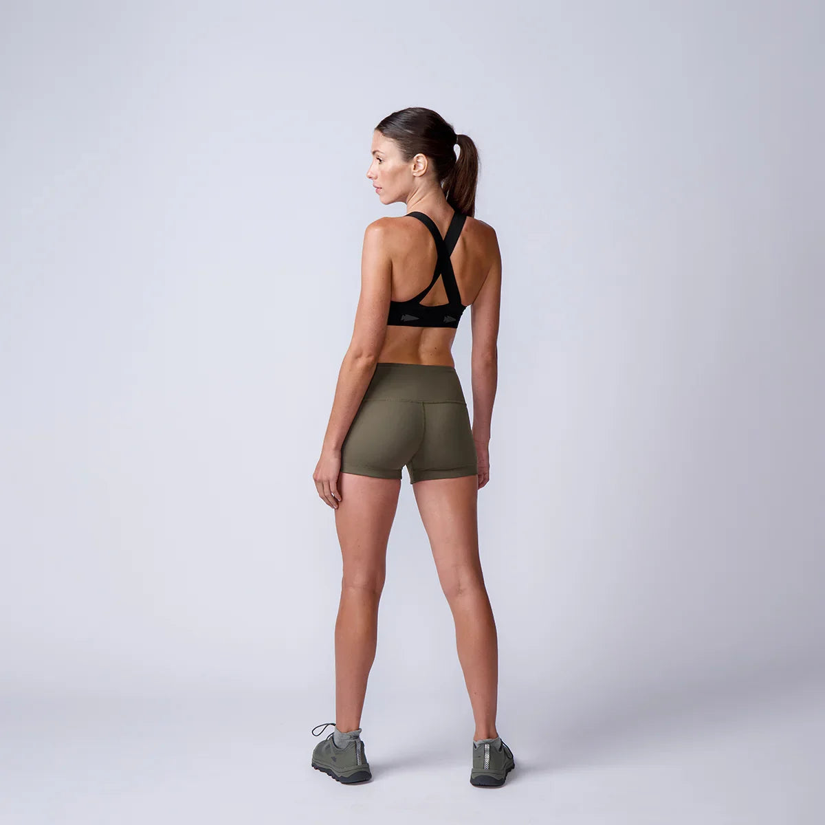 Woman wearing GORUCK olive green athletic shorts and black sports bra, standing in studio