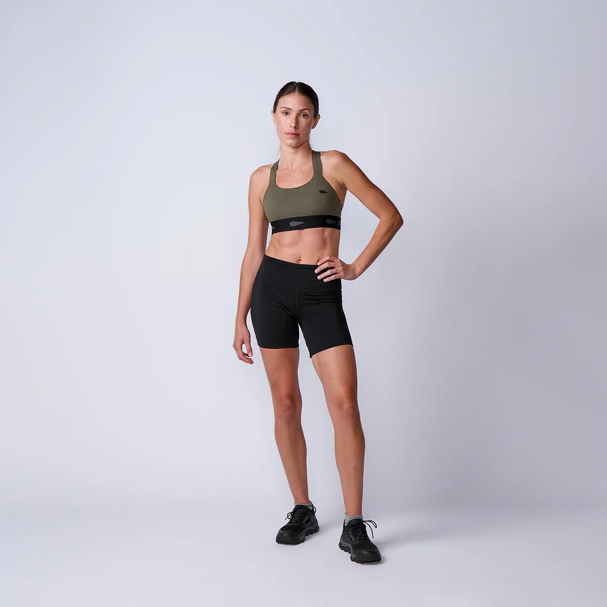 Woman wearing GORUCK olive sports bra and black shorts in studio for rucking gear showcase