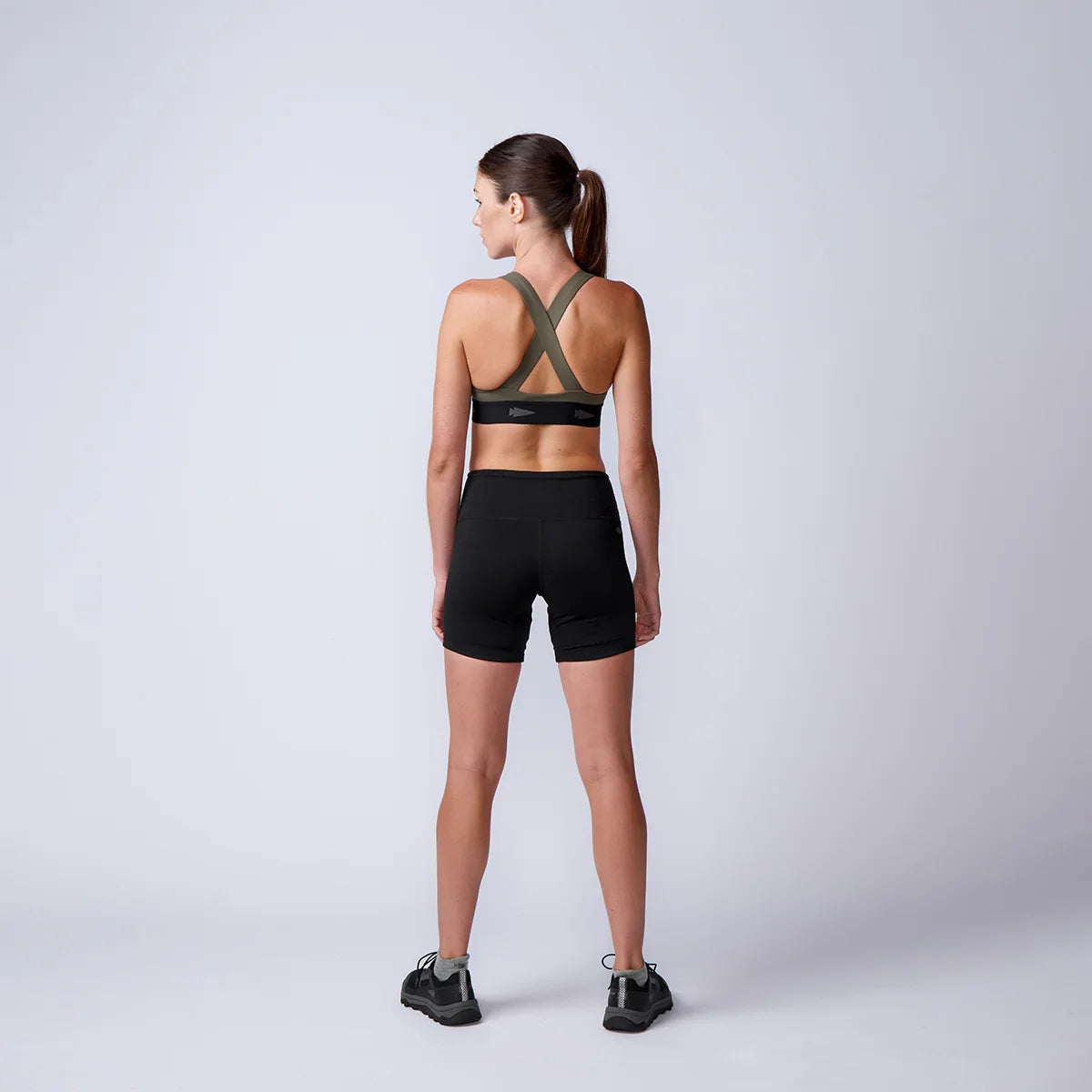 Woman in GORUCK rucking sports bra and shorts, back view, in minimalist studio setting