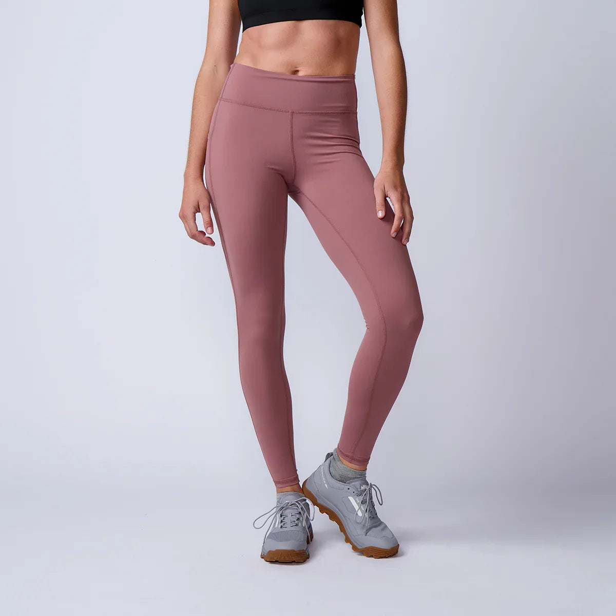 Woman wearing mauve GORUCK athletic leggings and gray sneakers, studio background