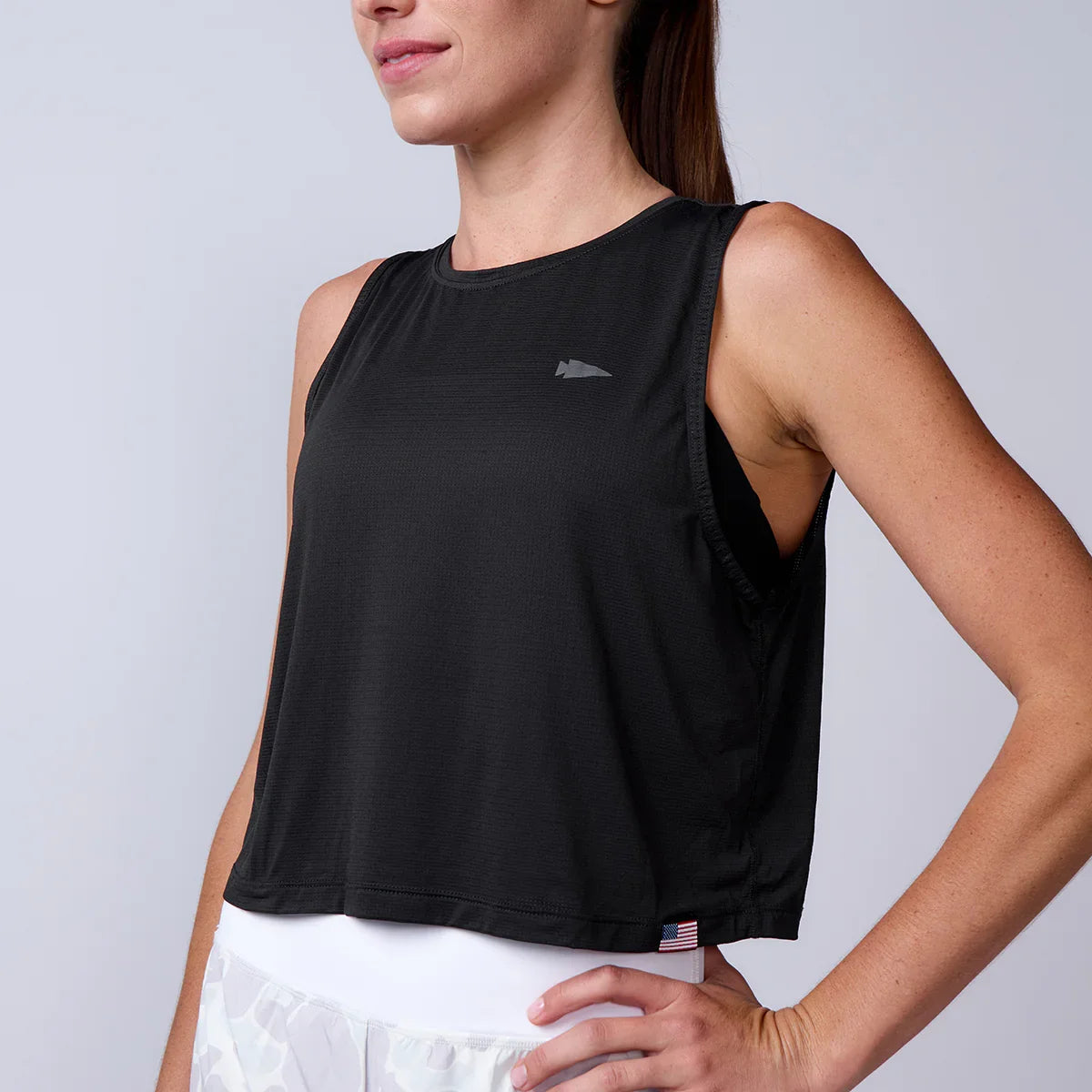Woman wearing a GORUCK black sleeveless crop top with logo and American flag tag