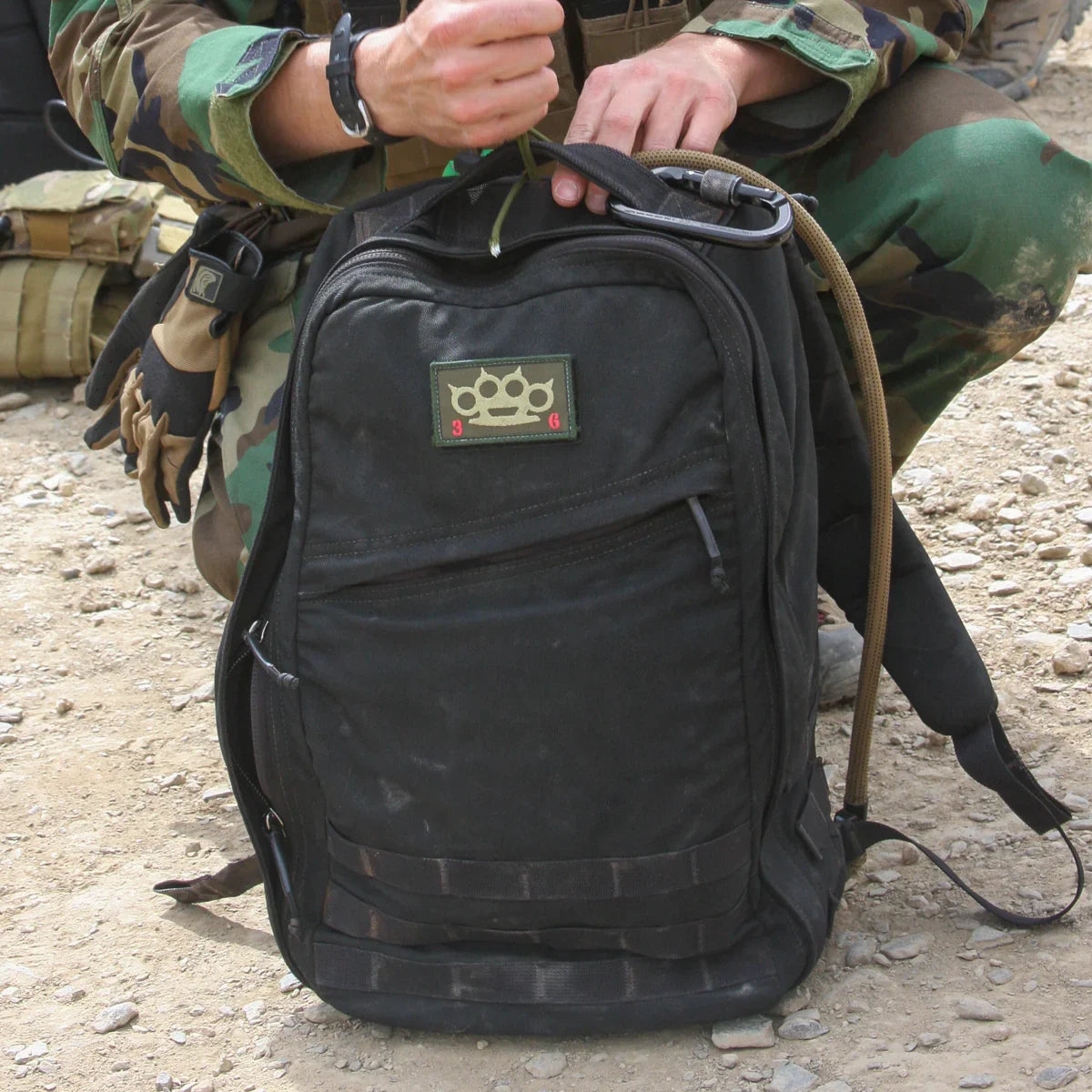 GORUCK black rucksack on rocky ground, held by person in camouflage, outdoor gear visible