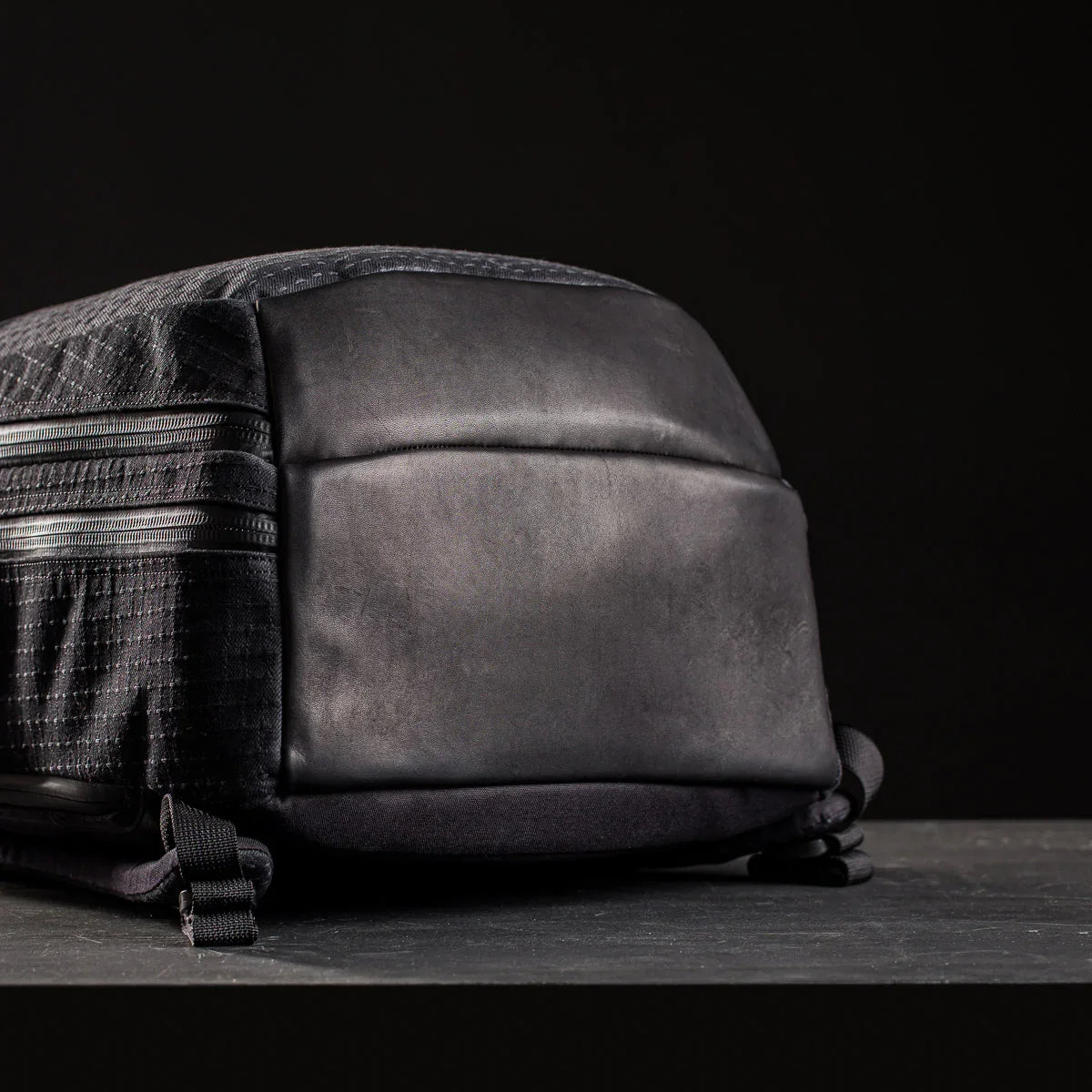 GORUCK black rucking backpack with rugged leather bottom and zippered side pockets on dark background