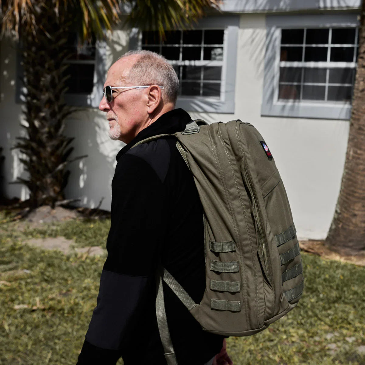 Man outdoors wearing a GORUCK GR2 40L Ranger Green rucksack in front of a house