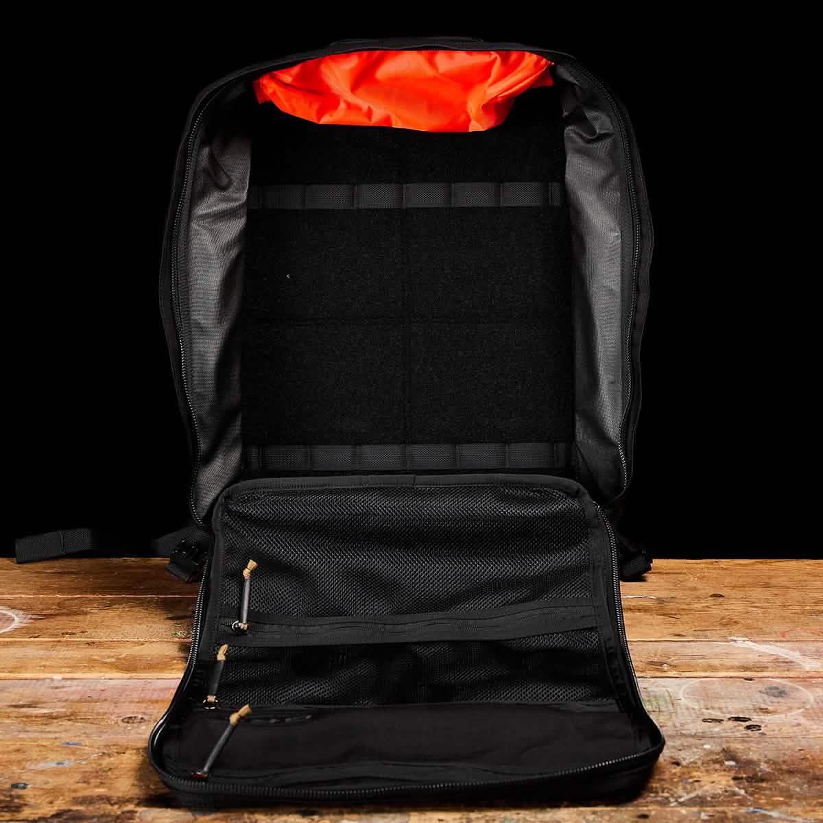 GORUCK GR3 black rucksack open on a wooden table, showing internal compartments and bright orange lining.