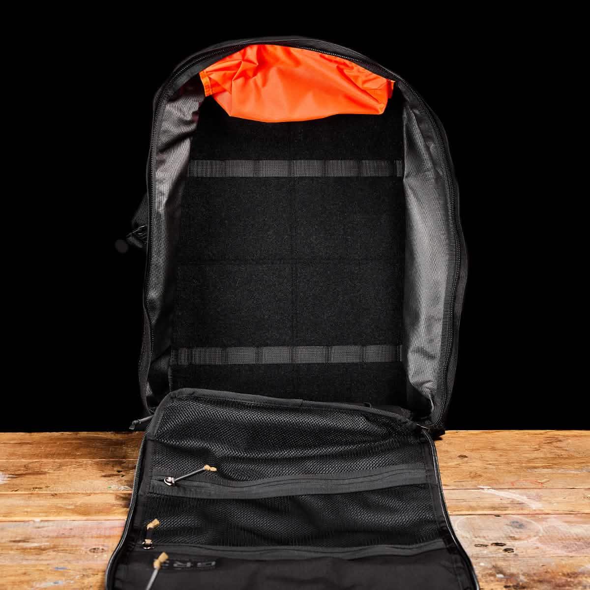 GORUCK open black rucksack on wood table, orange interior with mesh pockets, rugged gear
