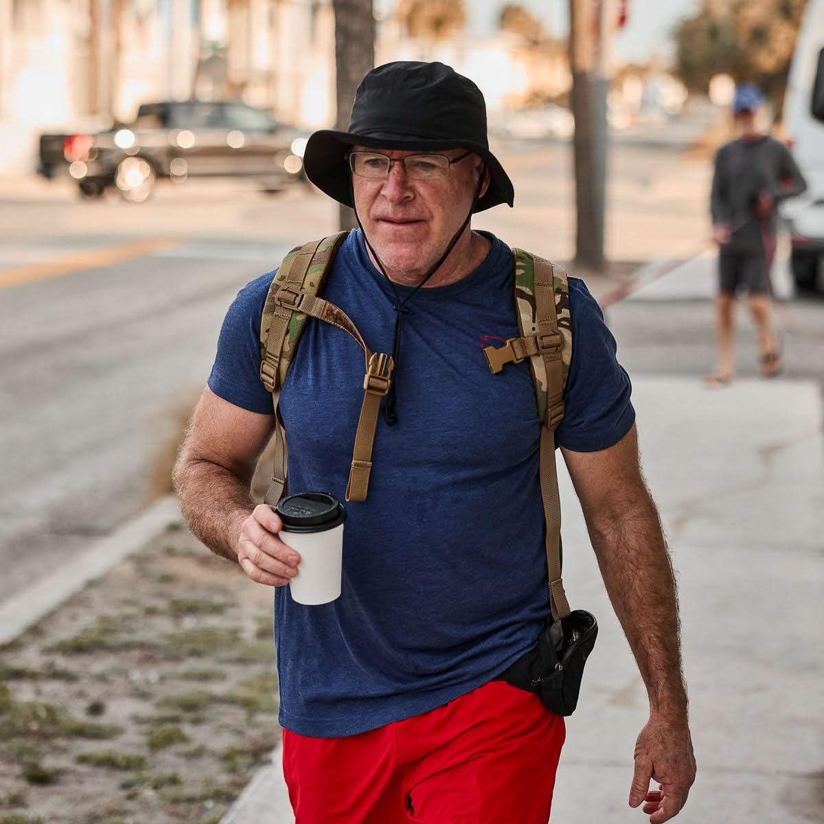 Man wearing GORUCK boonie hat, tactical backpack, and casual gear rucking on a city street