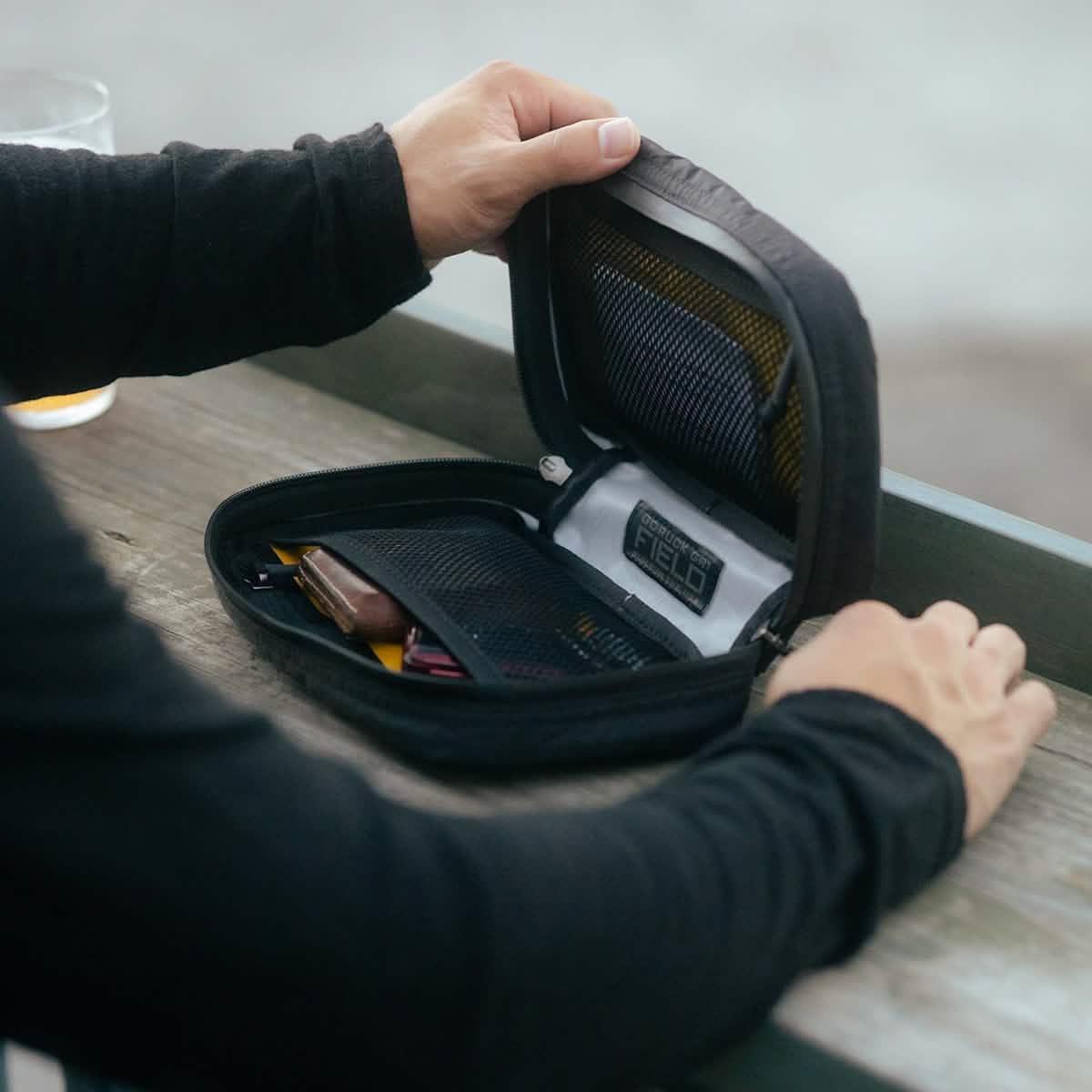 Person opening a GORUCK organizer pouch with gear inside on a wooden surface