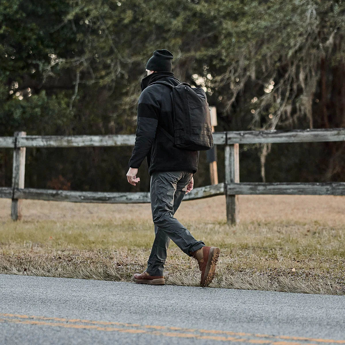 Man rucking with GORUCK backpack outdoors near wooden fence, wearing outdoor gear