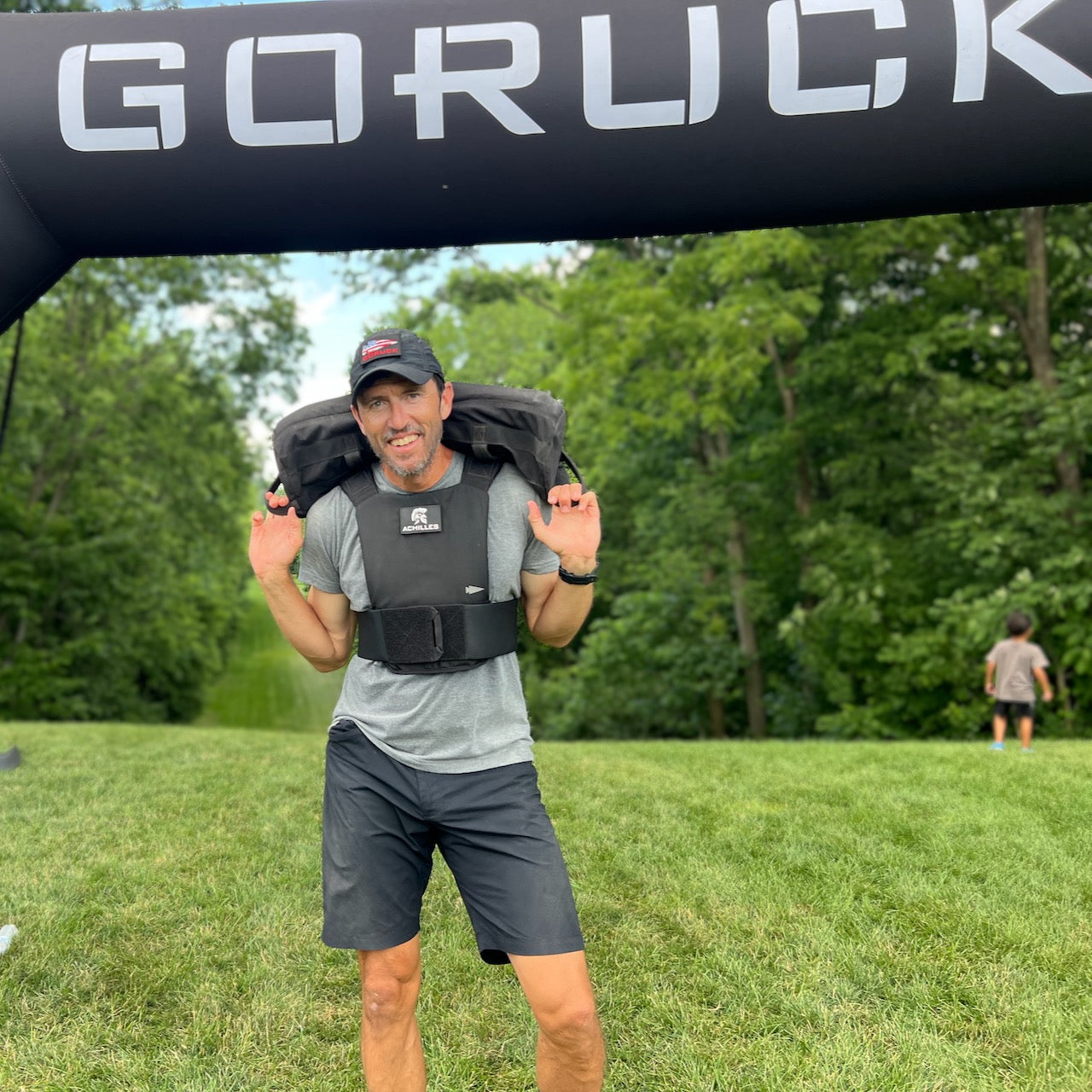 Man in athletic gear wears the Three Rules Tee - Unisex Tri-BlendX, carrying weight under a GORUCK arch outdoors—proving you can look cool and stay on track while pushing your limits.