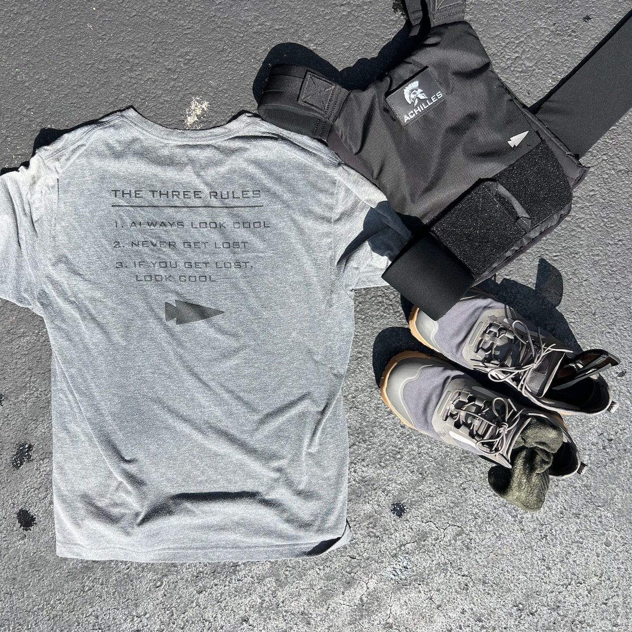 A gray Three Rules Tee - Unisex Tri-BlendX, black weighted vest, and gray sneakers are laid out on a sunny outdoor surface—gear that keeps you looking cool wherever your workout takes you.