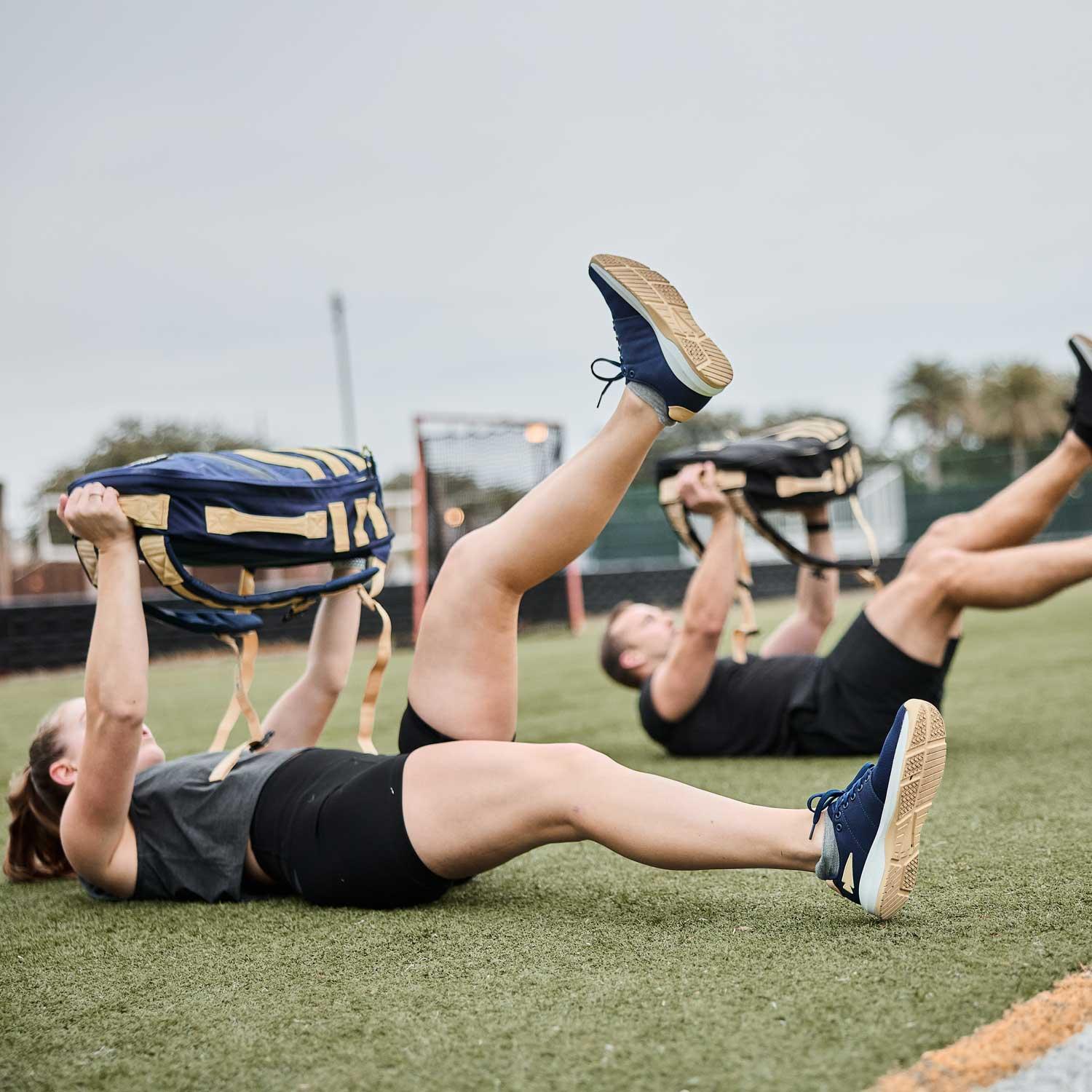 Two people rucking with GORUCK sandbags while exercising on a turf field outdoors