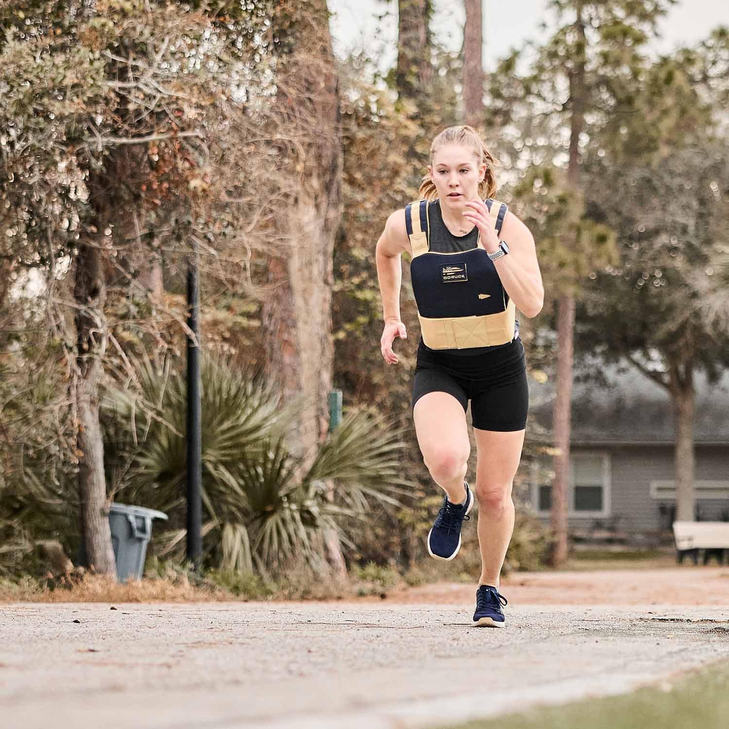 Woman running outdoors in GORUCK weighted vest and shorts during rucking workout