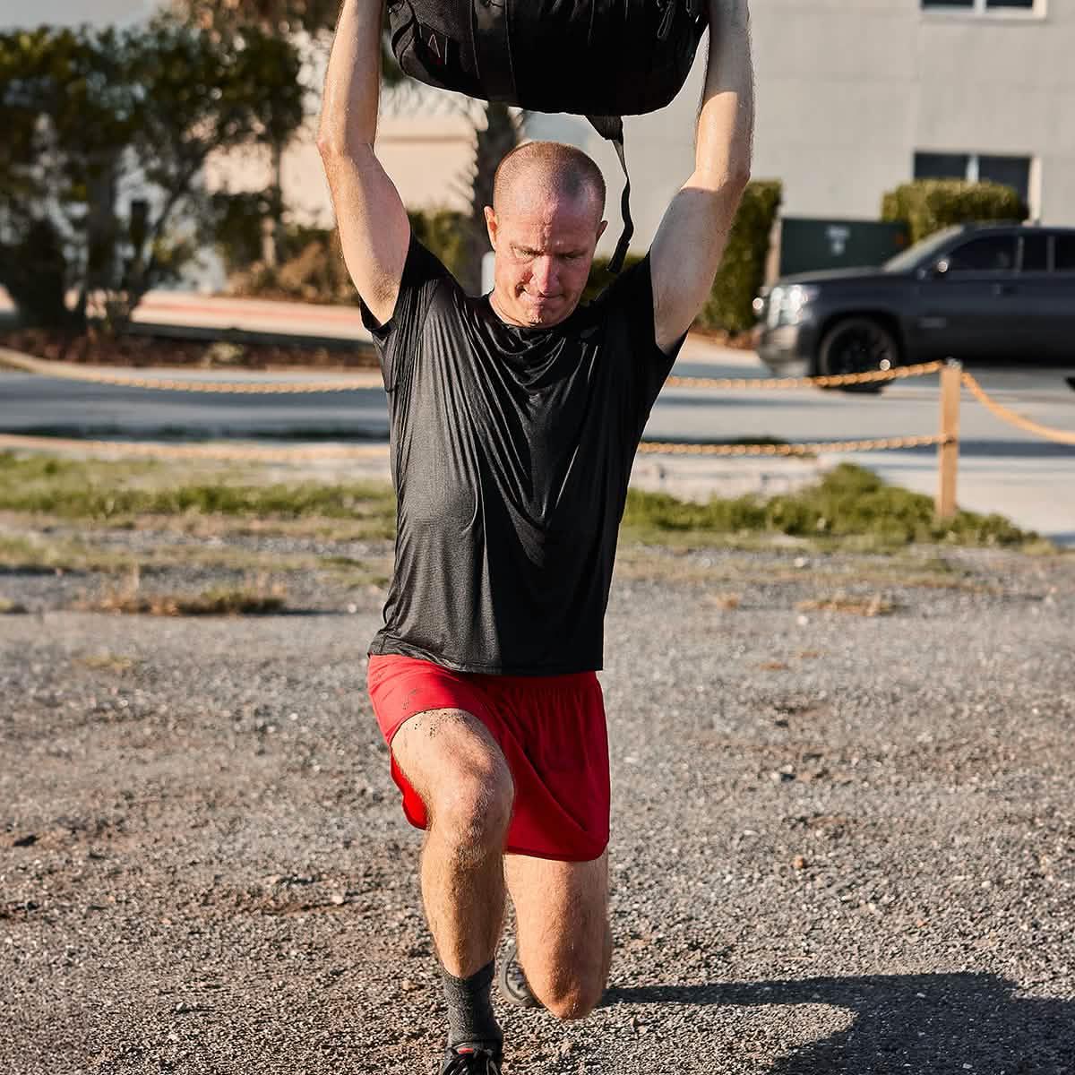 Man rucking outdoors doing overhead lunge with weighted rucksack, wearing GORUCK gear