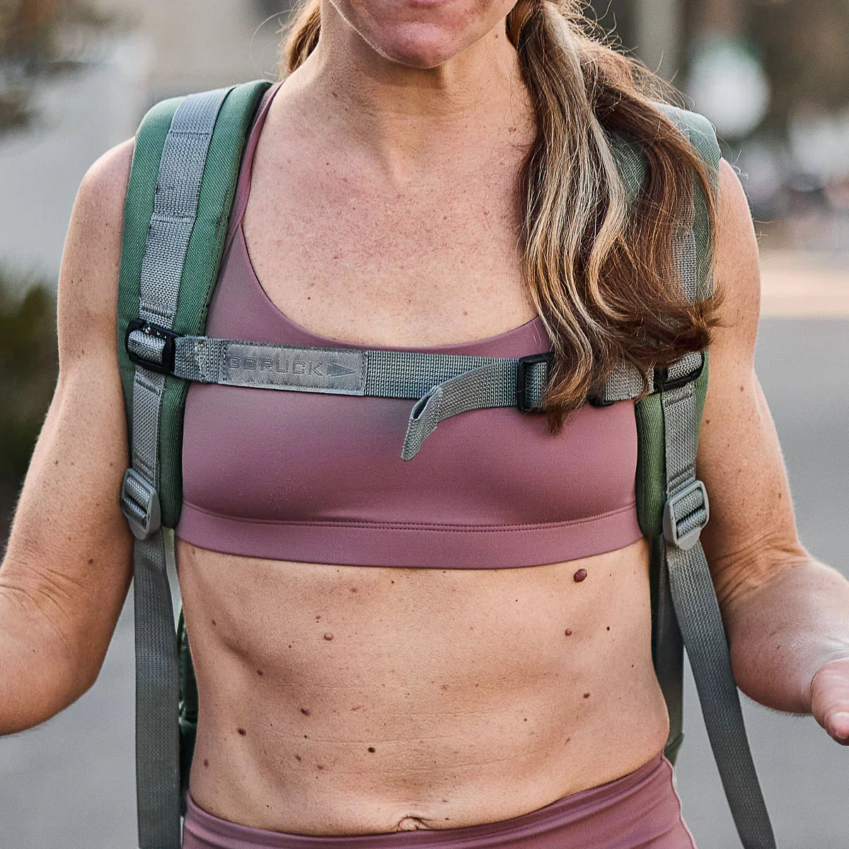 Woman wearing GORUCK Stealth Bra in Desert Rock color with rucksack, outdoor fitness setting