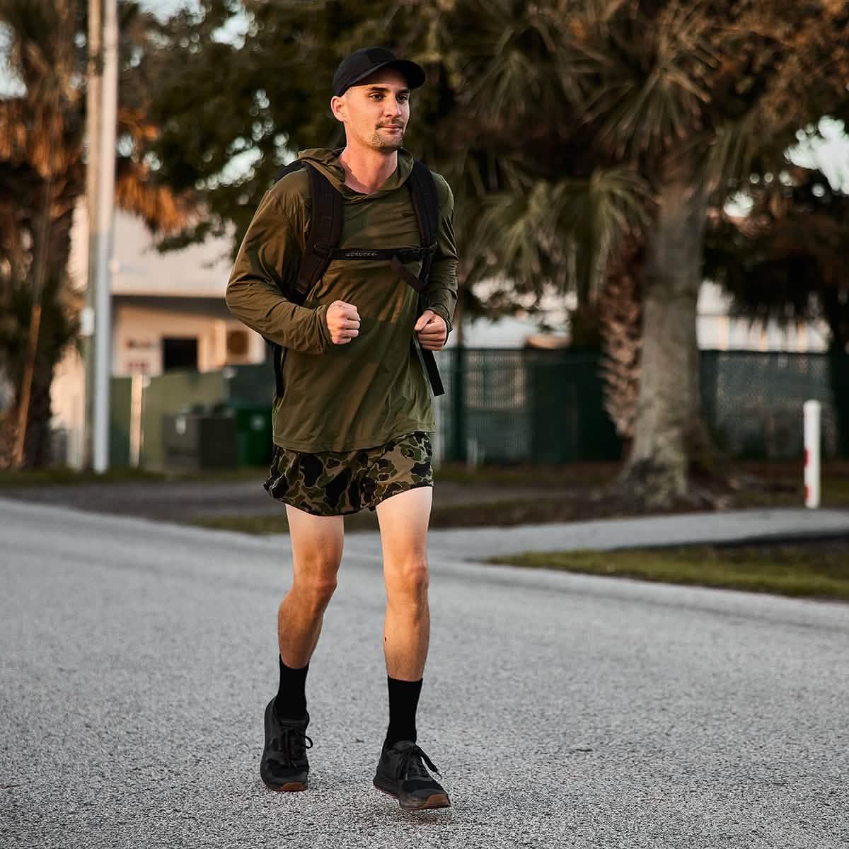 Man rucking outdoors wearing GORUCK Ranger Panties camo shorts, backpack, and black cap