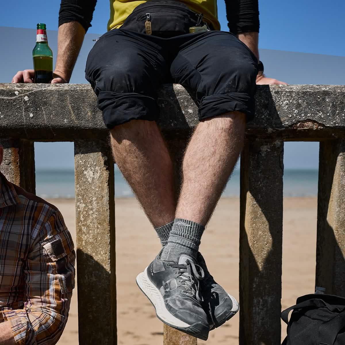 Man wearing GORUCK charcoal Merino wool socks and sneakers sitting on a beach wall