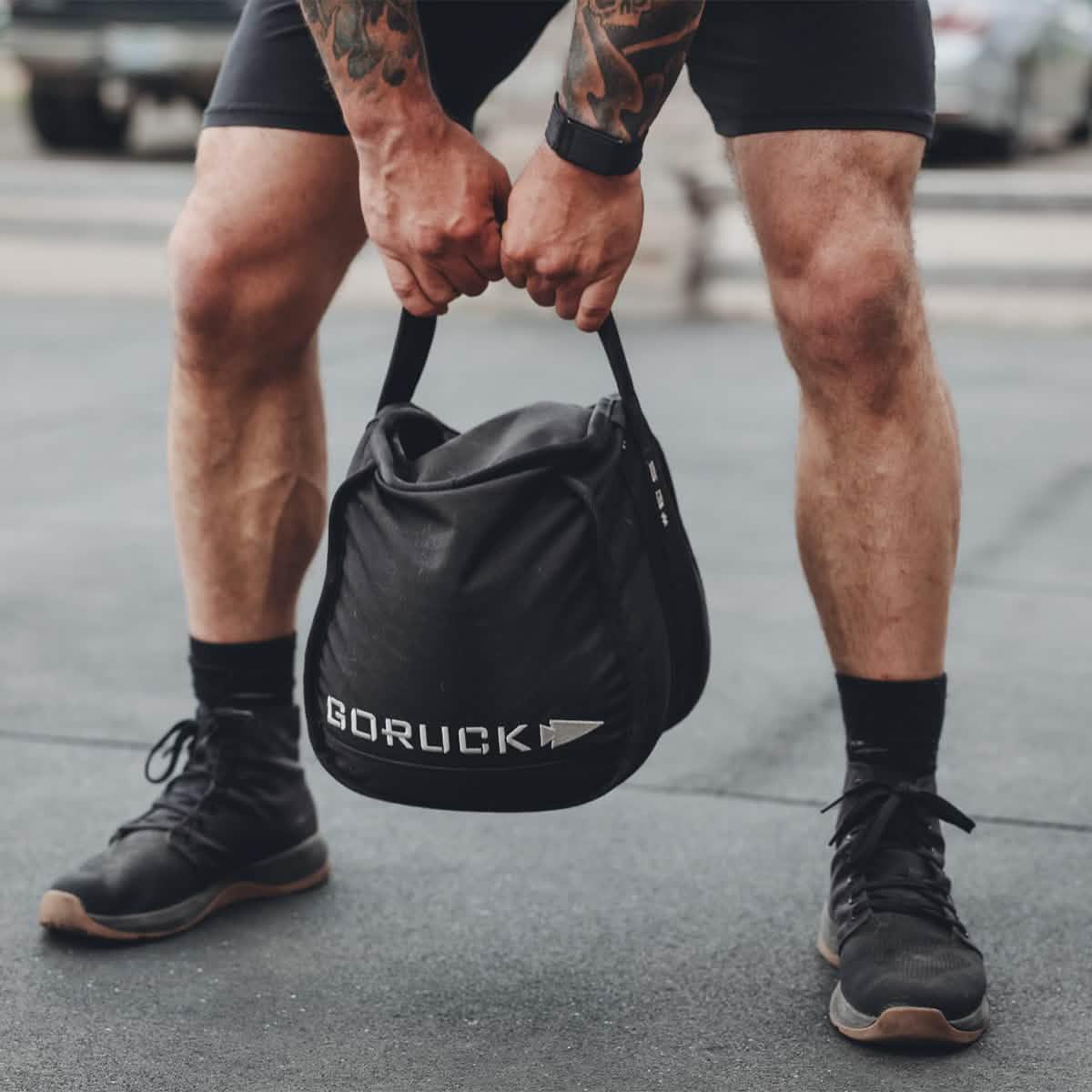Man holding GORUCK rucking sandbag outdoors, athletic gear and fitness training.
