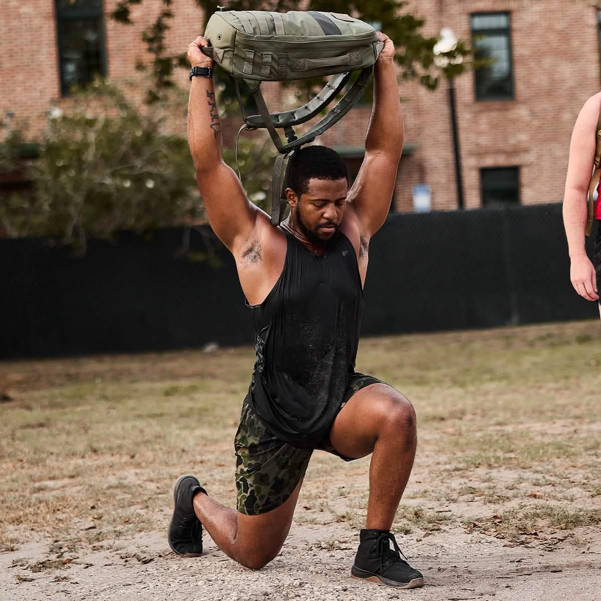 Man performing outdoor ruck workout with GORUCK backpack overhead on one knee