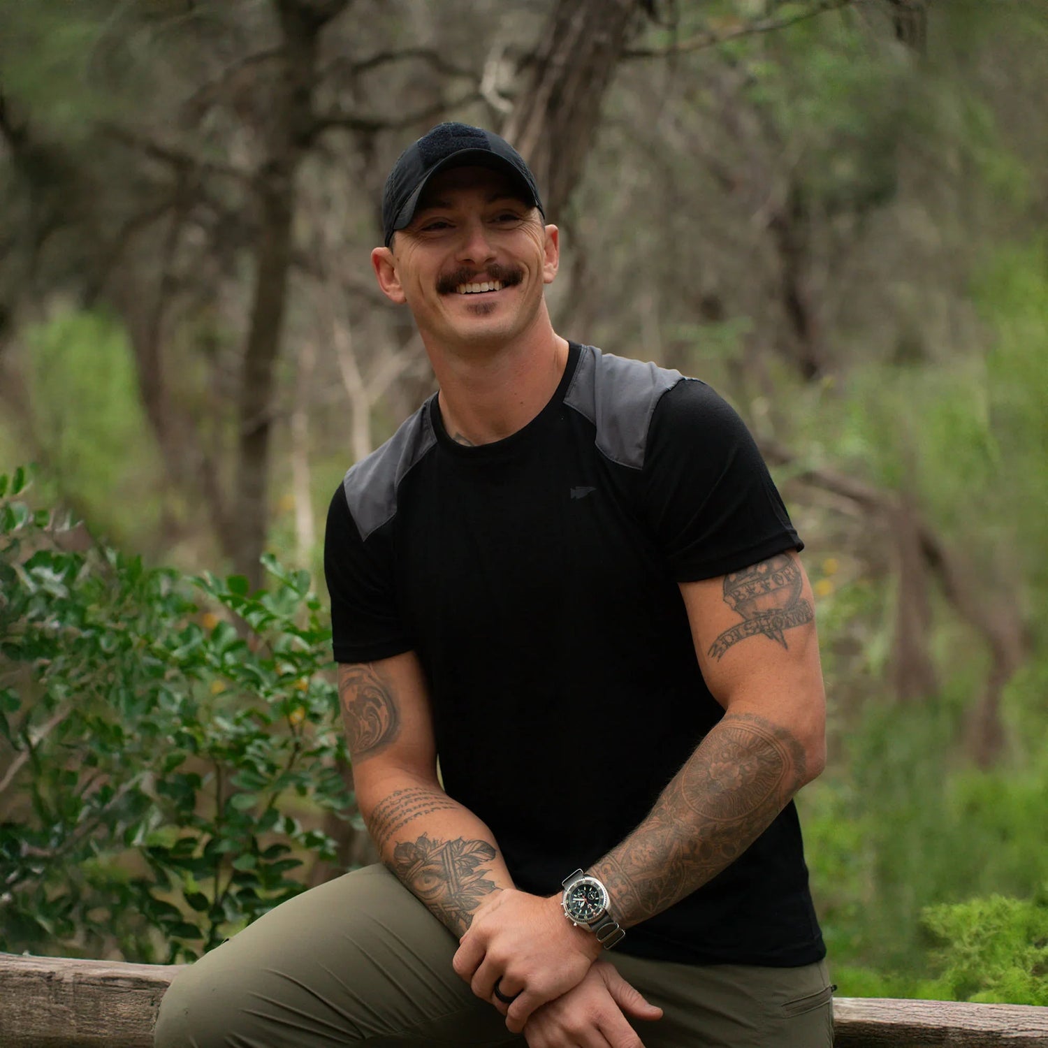 Man in GORUCK athletic gear with tattoos, smiling outdoors in a forest setting
