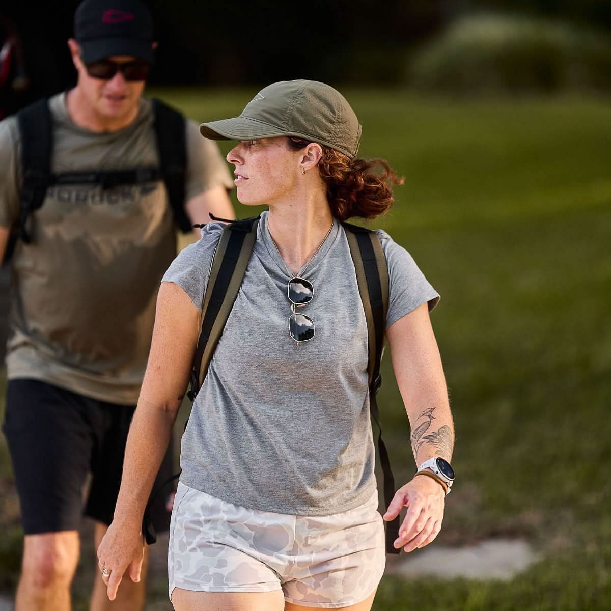 Woman rucking outdoors wearing GORUCK gear, backpack, and cap on grassy path