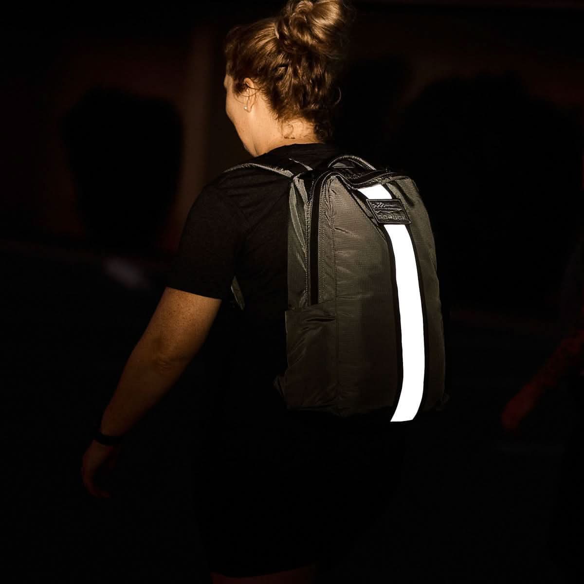 Person wearing GORUCK backpack with reflective stripe at night, rucking gear for safety.