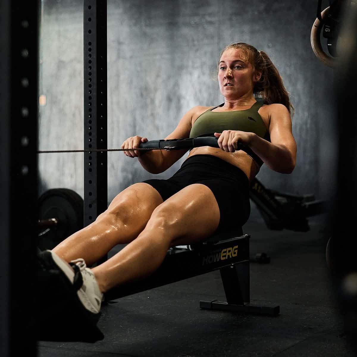 Woman wearing GORUCK Tough Flex Ranger Green sports bra rowing on exercise machine in gym