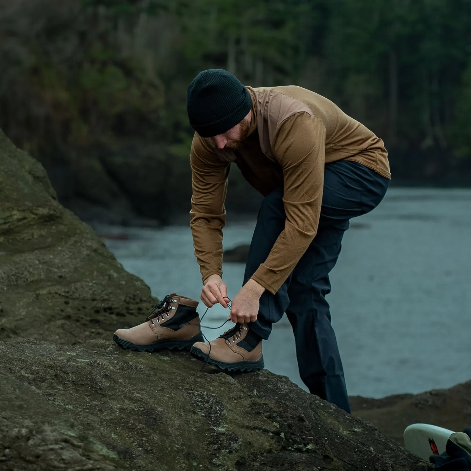Man tying GORUCK rucking boots on rocky riverside, outdoor adventure gear