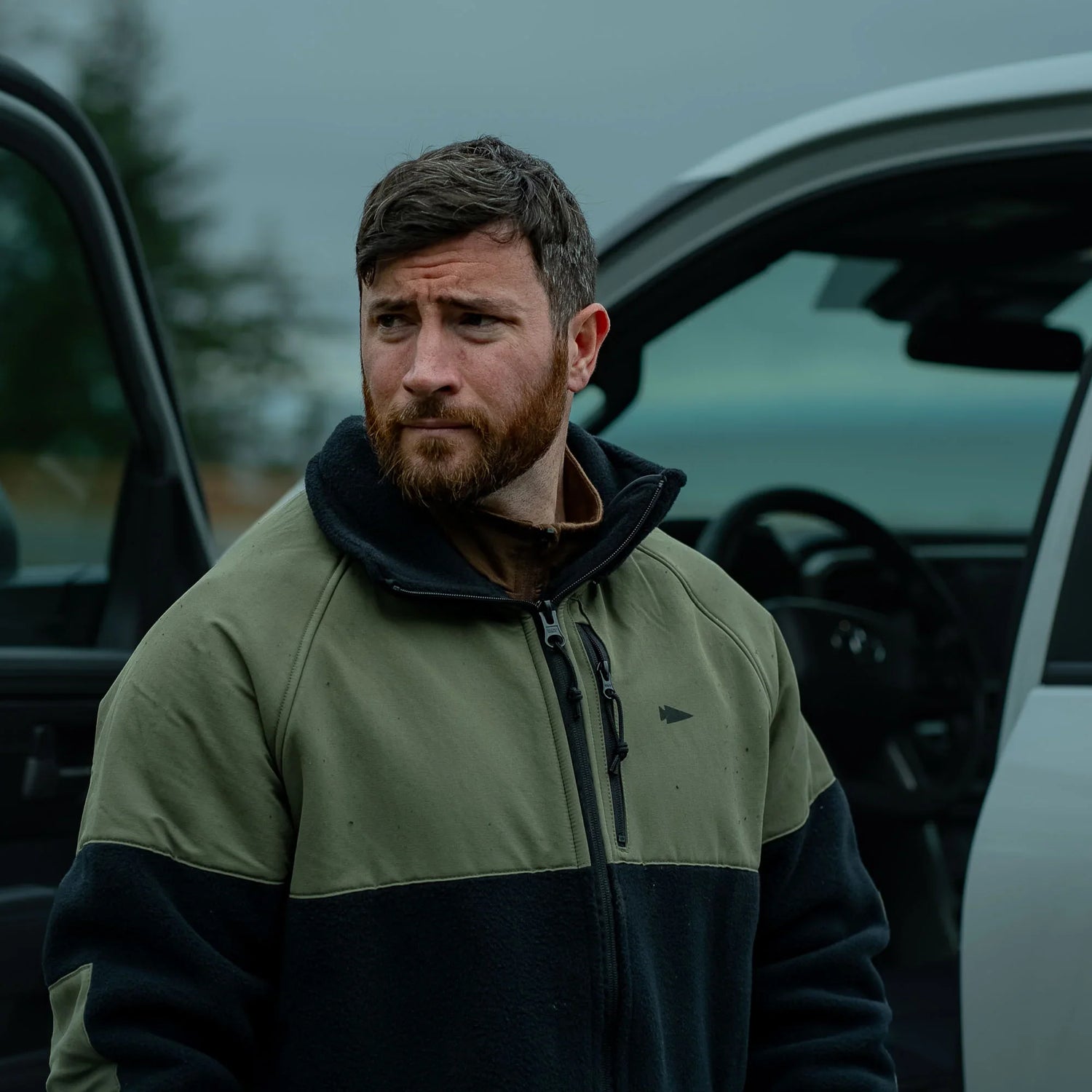 Man in GORUCK jacket standing outdoors by open car door, rugged and ready for adventure