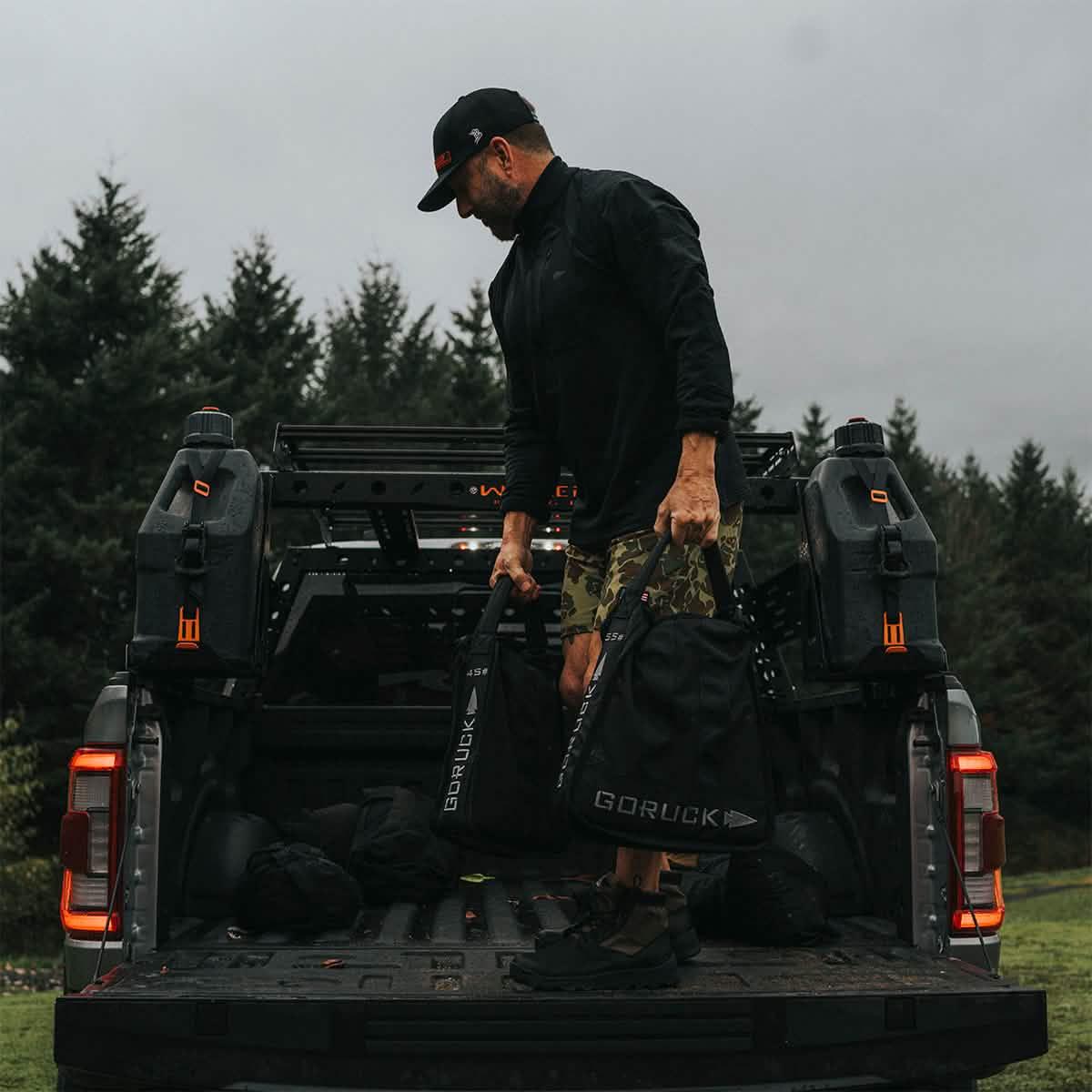 Man loading GORUCK sandbags and gear onto truck bed outdoors, featuring rugged rucking equipment.